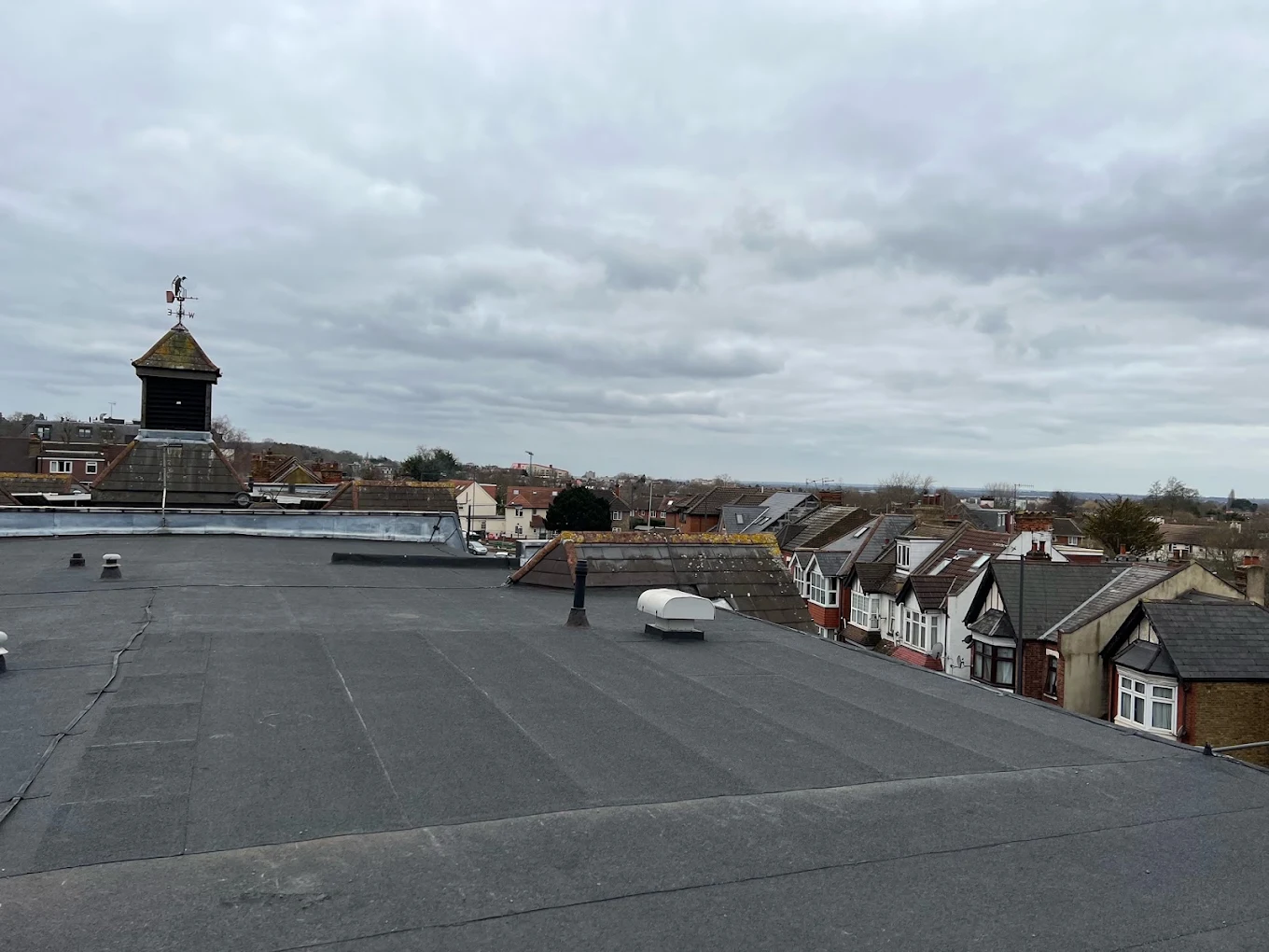 Wide expanse of felt flat roof over a commercial building, with rooftops behind