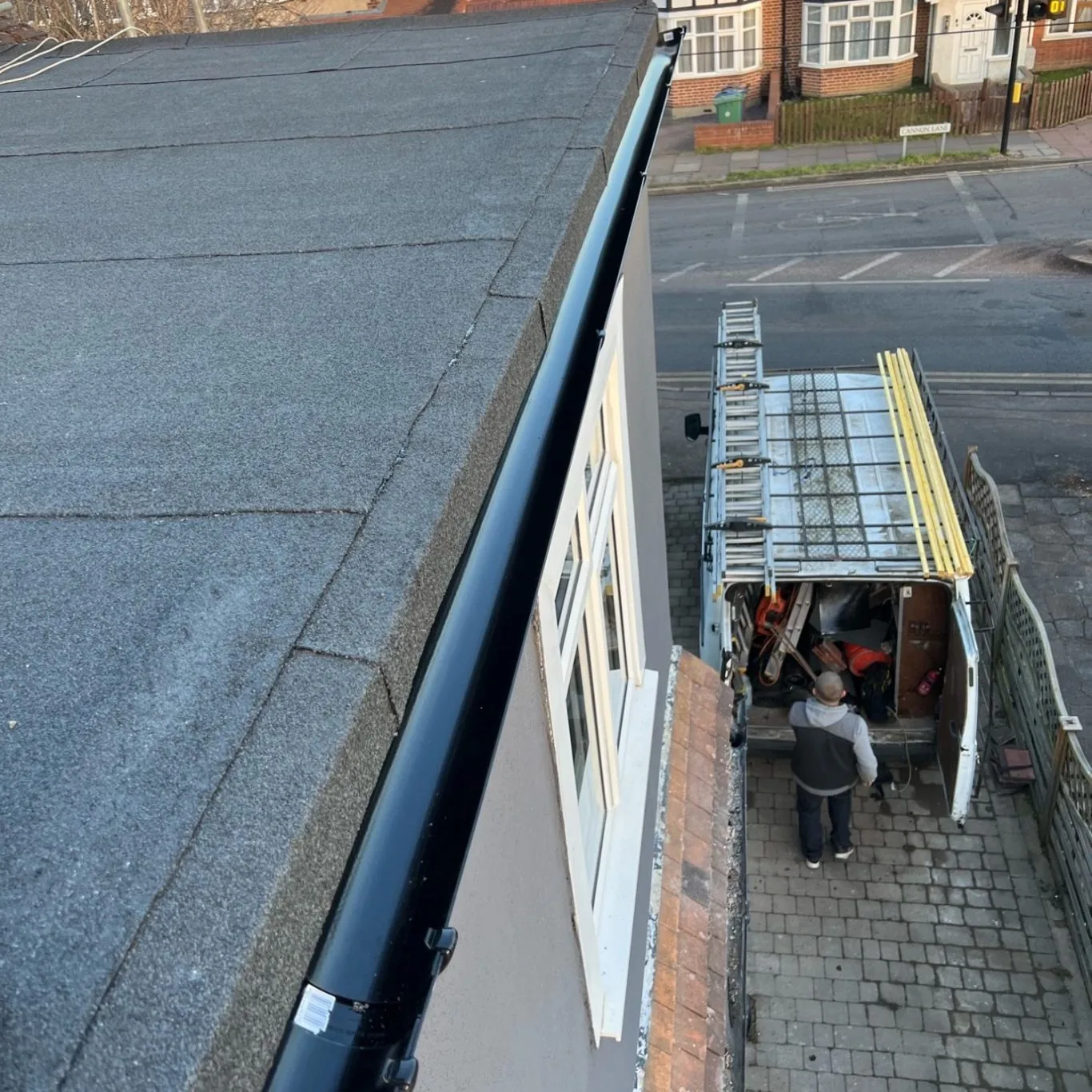 Felt flat roof edged with black guttering, the works van parked on the street below